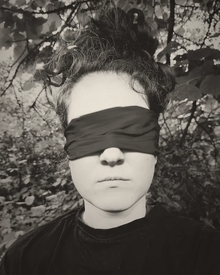 Portrait en noir et blanc d'Erika Wild, les yeux bandés, debout dans les feuillages